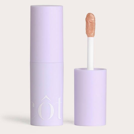 Côte Beauty The Necessity Peptide Lip Shine Euphoria Shimmer Nude Non-Toxic Lip Gloss tube with an open cap beside it. 